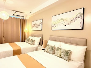 A hotel room with two beds, a large window with curtains, an air conditioning unit, and two framed artworks on the wall. - Cozy 1-bedroom condo in peaceful Pasay City with AC (Pasay City)