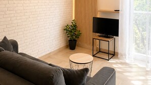 Ein modernes Wohnzimmer mit Ziegelwand, einer Couch, einem Fernseher auf einem Schrank, einer Topfpflanze und einer Pendelleuchte.