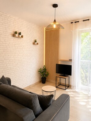 A modern living room with a brick wall, a sofa, a TV on a stand, a potted plant, and a pendant light. - Large Studio in residence with swimming pool (Provence-Alpes-Côte d'Azur)