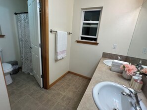 A bathroom with a toilet, shower, sink, and a window.