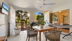 Een balkon met een tafel, stoelen, een barbecue en een hangmat.