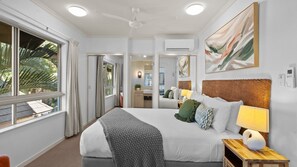 Ein Hotelzimmer mit Bett, Nachttisch, Lampe und einem großen Fenster mit Vorhängen.