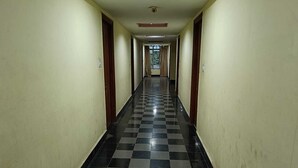 Un pasillo largo y estrecho con suelo a cuadros en blanco y negro, puertas de madera a ambos lados y un techo con iluminación empotrada.