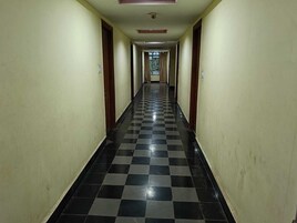 A long, narrow hallway with checkered black and white flooring, wooden doors on both sides, and a ceiling with recessed lighting.
