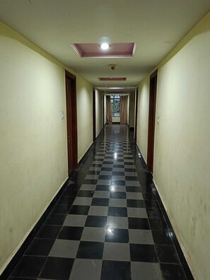 Un pasillo largo y estrecho con piso a cuadros negro y blanco, puertas a ambos lados y una lámpara en el techo.