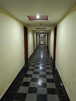 A long, narrow hallway with checkered black and white flooring, doors on both sides, and a ceiling light.