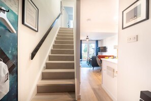 Eine Treppe führt zu einem Wohnbereich mit einem Sofa, einem Esstisch und einem an der Wand befestigten Fernseher.