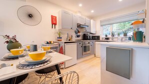 Een moderne keuken met witte kastjes, een eettafel met gele en blauwe borden, en een klein aanrecht met een spoelbak.