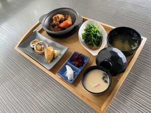 A tray with sushi, a bowl of soup, a plate of greens, and a small dish of pickled vegetables.