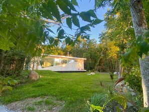 Una casa moderna con facciata in vetro, immersa in un prato curato e alberi.