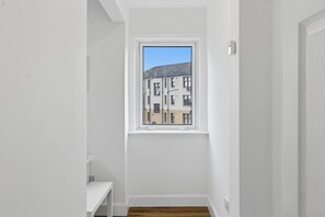 A narrow hallway with a window, a white wall, and a wooden floor. - The Provost Apartment (Dundee)