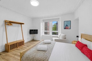 A bedroom with a bed, a wooden bench, a TV, a window, and a painting. - The Provost Apartment (Dundee)