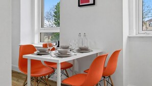 A dining area with a white table set for four, orange chairs, and a framed artwork on the wall.
