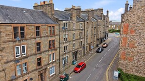 A street lined with stone buildings, a red car parked on the side, and a clear blue sky.