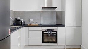 A modern kitchen with white cabinetry, a black countertop, a built-in oven, and a stainless steel refrigerator.