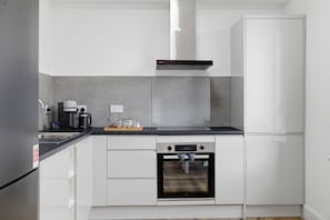 A modern kitchen with white cabinetry, a black countertop, a built-in oven, and a stainless steel refrigerator. - The Provost Apartment (Dundee)