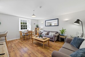 Ein geräumiges Wohnzimmer mit Holzboden, einem grauen Sofa, einem Couchtisch und einem Essbereich mit Holzsesseln und einem Tisch.