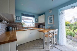 A kitchen with white cabinets, a wooden countertop, a window with a view, and a dining area with white chairs. - Fife Cottage between St Andrews and Dundee (Fife)