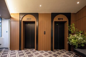 An elevator area with two elevators, a patterned carpet, and a potted plant. - MOTRI HOTEL Futian Huaqiang North Branch (Shenzhen)