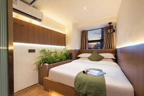 Quarto de hotel com cama, janela com cortinas, ar condicionado, planta e vista para a cidade.