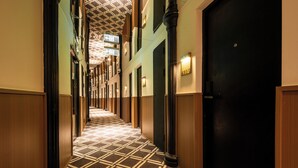En hotellkorridor med ett mönstrat golv, trädörrar och ett tak med ett geometriskt mönster.