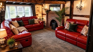 A cozy living room with two red leather sofas, a fireplace, and a large window with curtains. - Lilac Cottage (Henley-In-Arden)