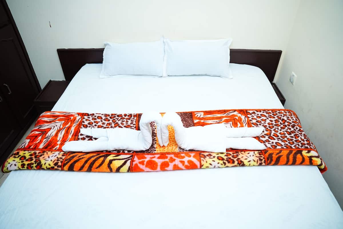 A neatly made bed with white pillows and a colorful blanket, a wooden headboard, and a plain wall.