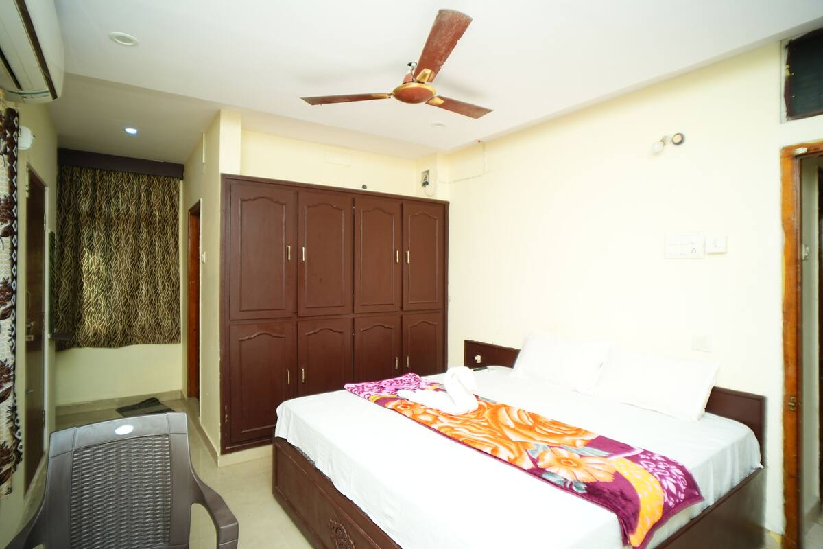 A bedroom with a bed, a wardrobe, a ceiling fan, and a chair.