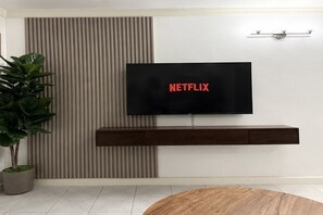 Ein modernes Wohnzimmer mit einem Wand-Fernseher, einer Holz-Unterhaltungseinrichtung und einem Blumentopf.