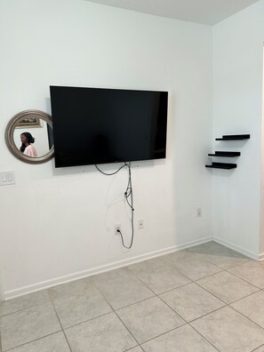 Ein Zimmer mit einem an der Wand befestigten Fernseher, einem Spiegel und einem Wandregal.