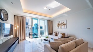 A modern living room with a sofa, a coffee table, a TV, and a city view through large windows. - Luxury 1BR Marina & Harbor View Beachfront (Dubai)