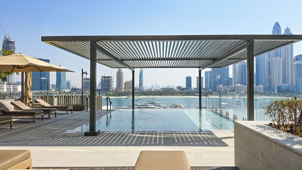 A rooftop infinity pool with a city skyline view, lounge chairs, and a pergola structure. - Luxury 1BR Marina & Harbor View Beachfront (Dubai)