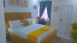 Habitación de hotel con cama, escritorio, silla, ventilador, puerta y planta en maceta.