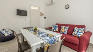 Ein kompakter Wohnraum mit Esstisch, rotem Sofa und einem an der Wand befestigten Flachbildfernseher.