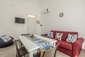 Un ambiente compatto con tavolo da pranzo, divano rosso e televisione a schermo piatto fissata al muro.
