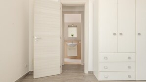 Ein Flur, der zu einem Badezimmer mit Waschbecken und Spiegel sowie zu einem Kleiderschrank mit mehreren Schubladen führt.