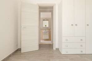 Ein Flur, der zu einem Badezimmer mit Waschbecken und Spiegel sowie zu einem Kleiderschrank mit mehreren Schubladen führt.