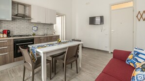 Eine kleine Küche mit modernen Geräten, ein Essbereich mit Tisch und Stühlen sowie ein rotes Sofa.