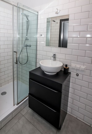 Un baño moderno con ducha acristalada, lavamanos blanco y tocador negro.