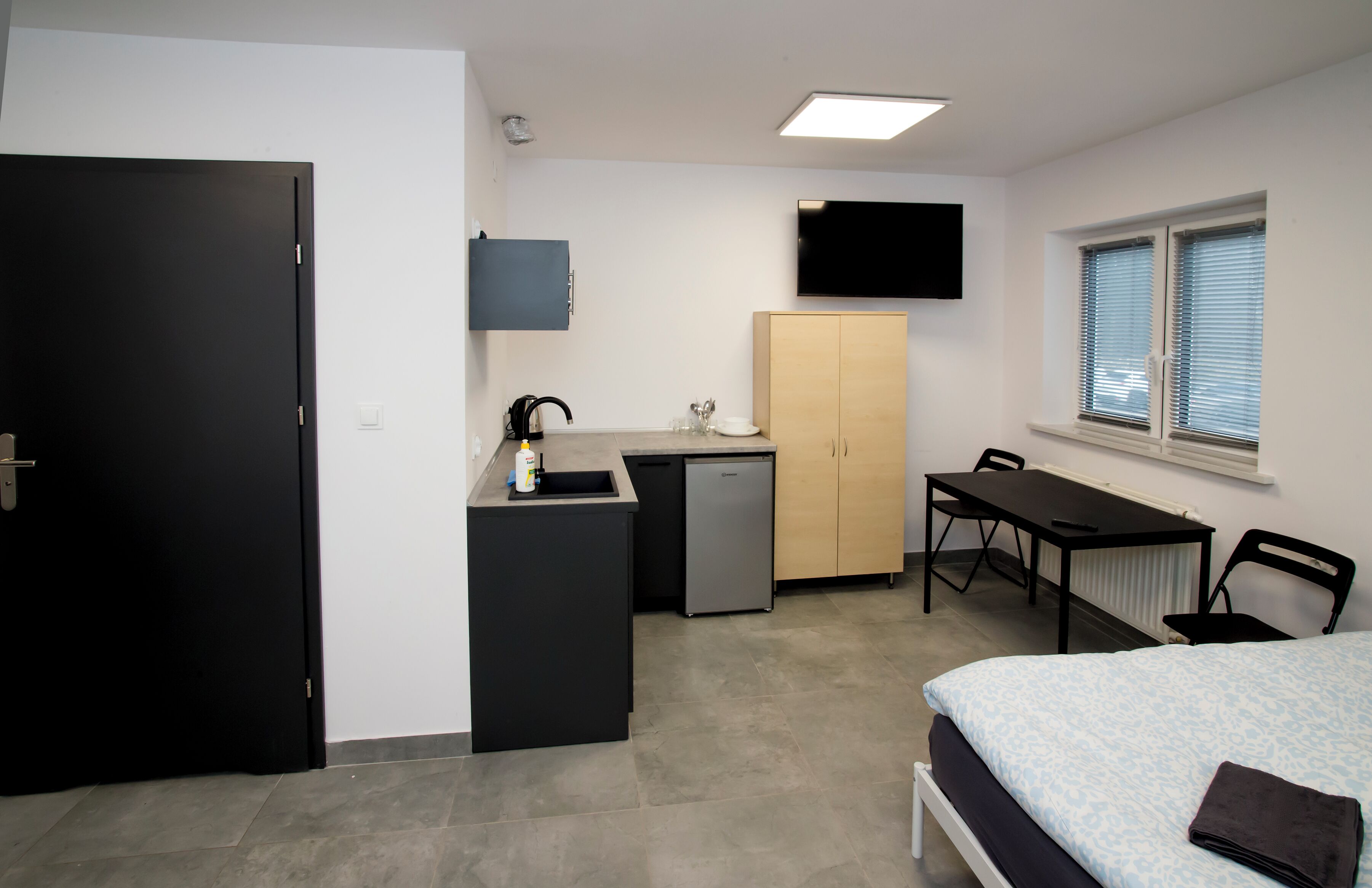 Una habitación compacta con cama, escritorio, kitchenette pequeño, televisión y ventana.
