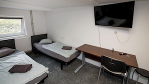 A dorm-style room with a bed, a desk, a chair, a TV, and a window. - Mia Mia House (Katowice)