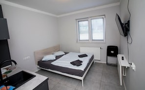 Un dormitorio con una cama, un escritorio, un radiador, una ventana y un televisor montado en la pared.