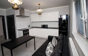 Una cocina moderna con armarios blancos, encimera negra y sofá negro con cojines estampados.