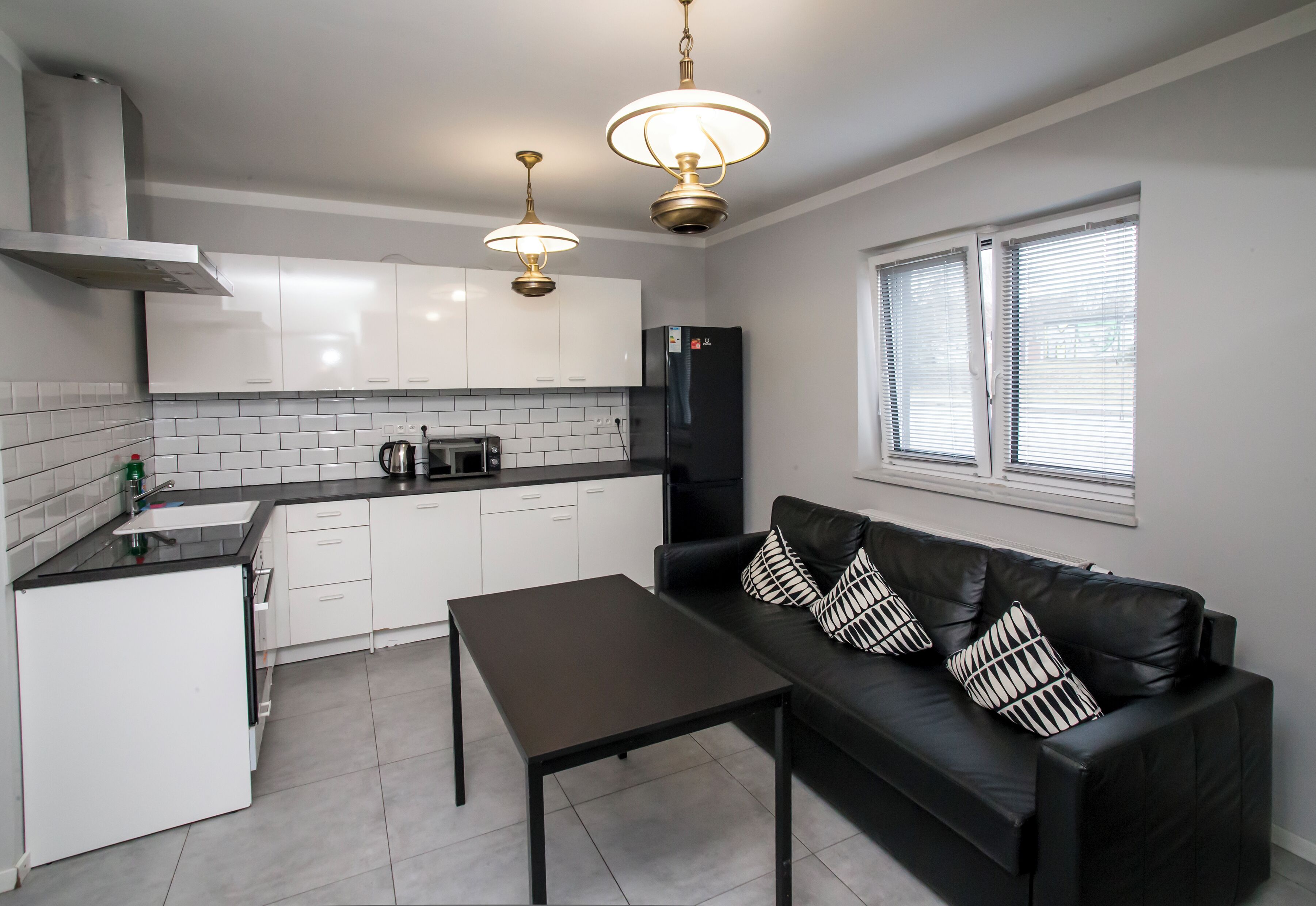 Una cocina moderna con armarios blancos, un refrigerador negro, una mesa de comedor y un sofá de cuero negro con cojines estampados.