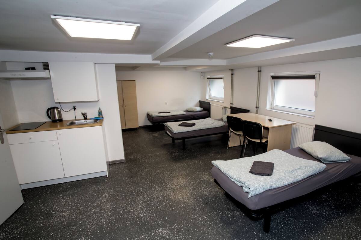 Une chambre compacte comprenant un coin cuisine, deux lits simples, un bureau et une chaise.