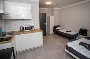 Habitación de hotel compacta con kitchenette, una cama individual, una mesita de noche y un armario.