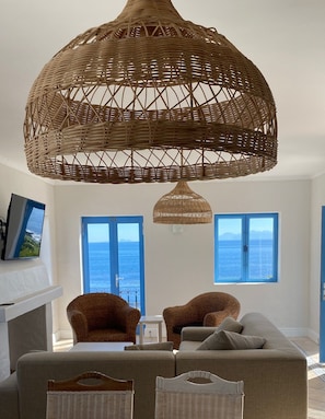 Ein modernes Wohnzimmer mit einer großen Korbschicht-Krone, zwei Korbstühlen, einem Sofa und einem Fernseher an der Wand.