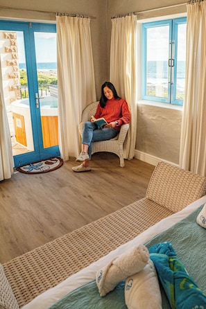 Ein Zimmer mit Meerblick, ein Korbstuhl, ein Bett und eine Tür zu einem Außenbereich.