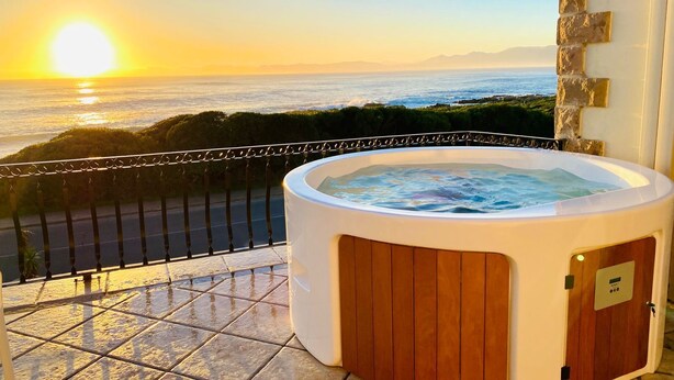 A hot tub on a balcony with a view of the ocean and mountains at sunset. - Casa Balena - The Seafront Whale House Experience (Gansbaai)