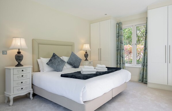 Une chambre à coucher comprenant un lit, deux tables de chevet, une fenêtre avec des rideaux et une armoire.